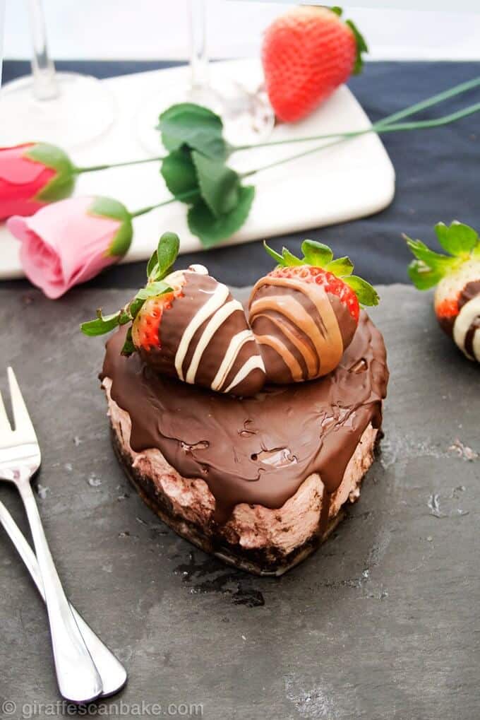 heart-shaped chocolate strawberry cheesecake for two beside two roses and two forks