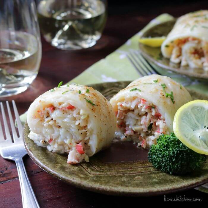 close-up of crab stuffed flounder on a plate with a fork and two wine glasses