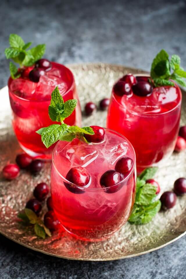 three glasses of cranberry gin cocktail on a gold serving platter garnished with mint