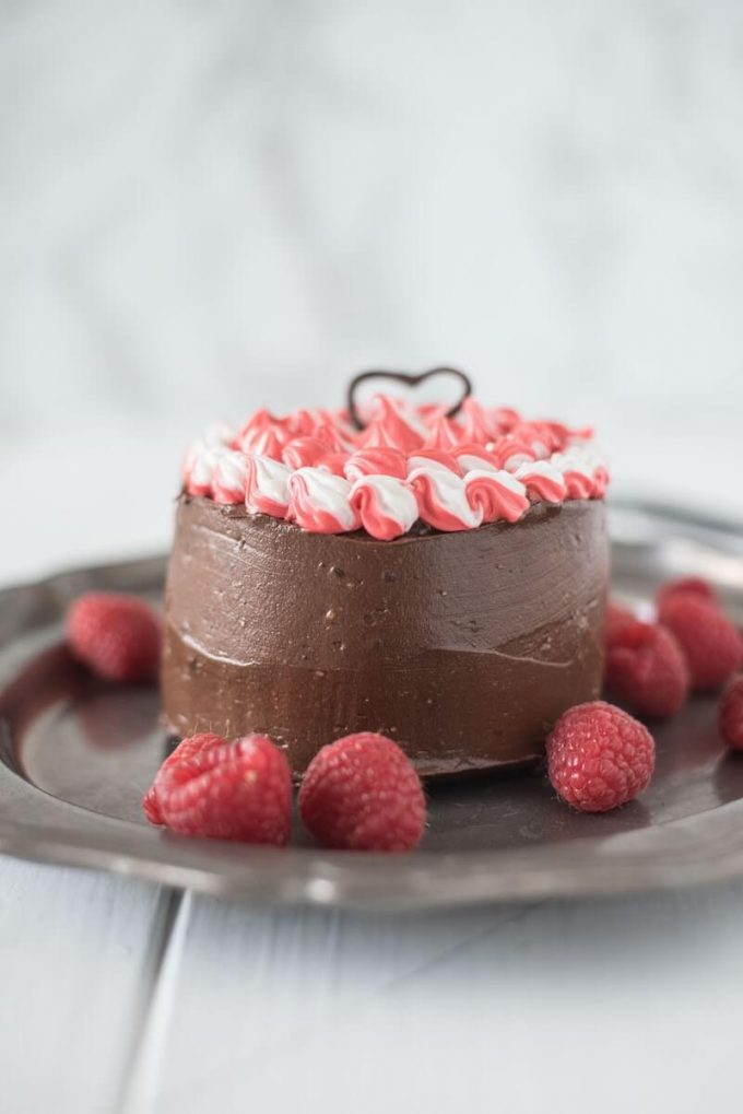 small mini chocolate cake with red and white icing on a plate with raspberries
