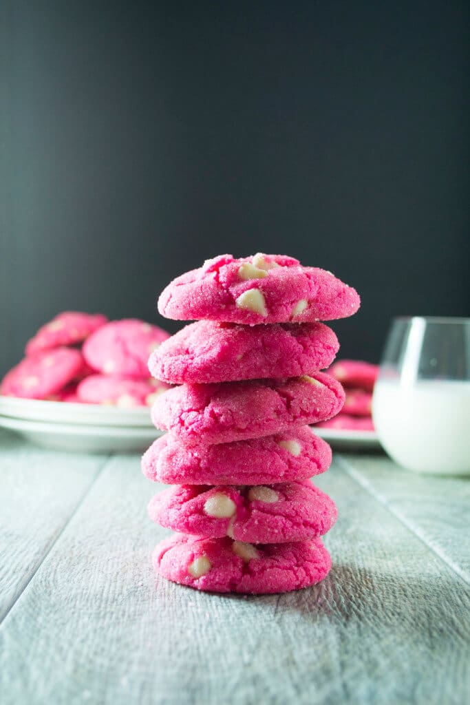 stack of six bright pink sugar cookies with a glass of milk in the background