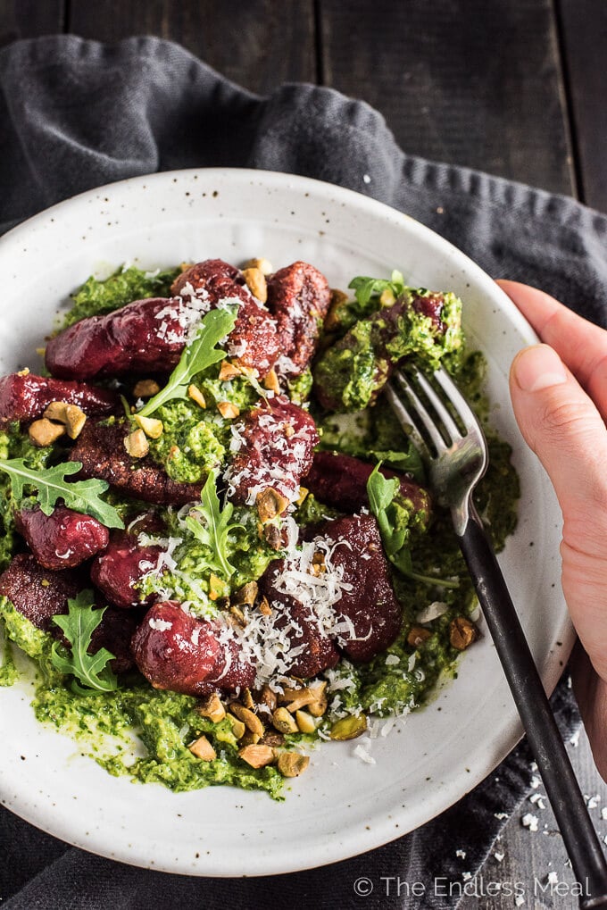 beet gnocchi with pesto arugula in a bowl with a fork