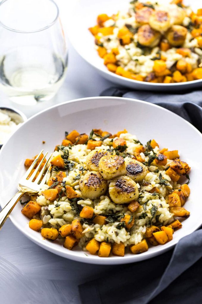 scallops with butternut squash risotto in a bowl beside glass of wine