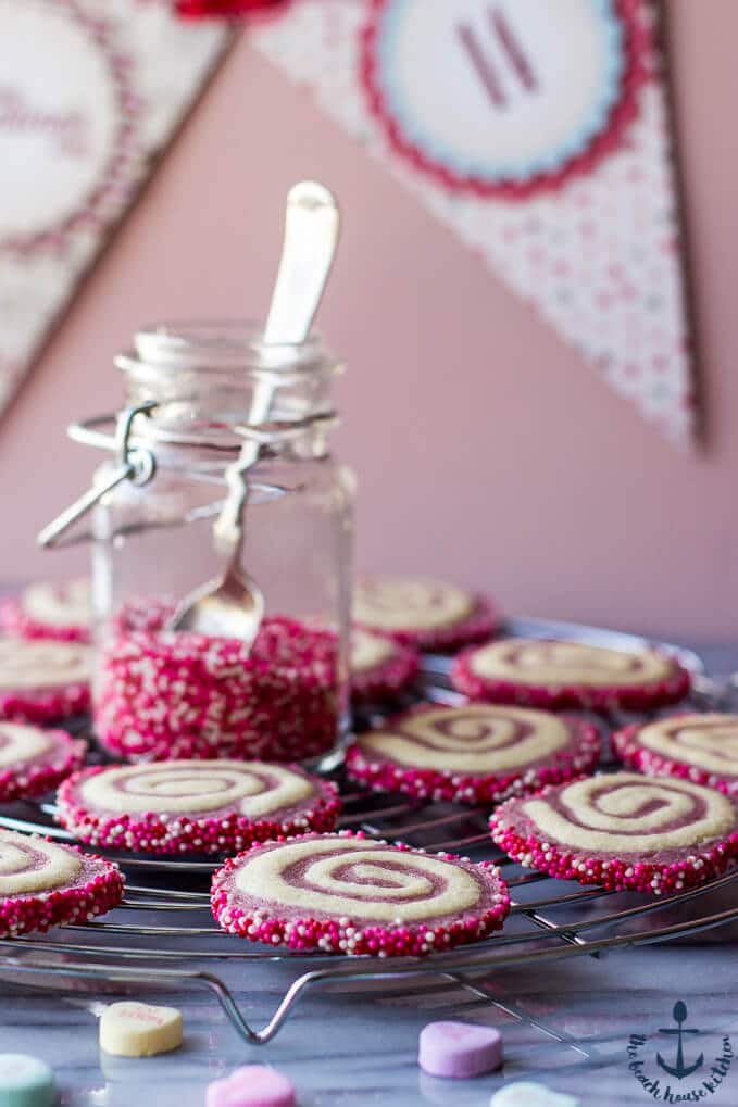 several valentine pinwheel cookies on a wire rack with jar of pink sprinkles and spoon