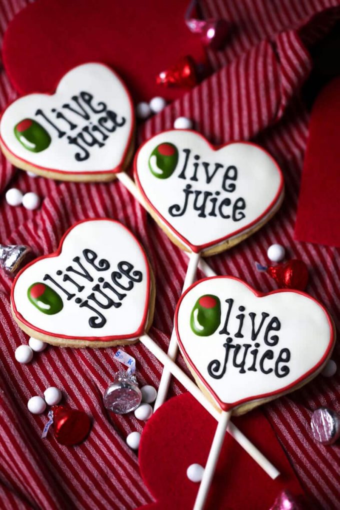 four valentine's day cookie pops that read olive juice in icing writing