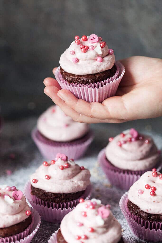 hand holding a cocoa cupcake with strawberry cream icing