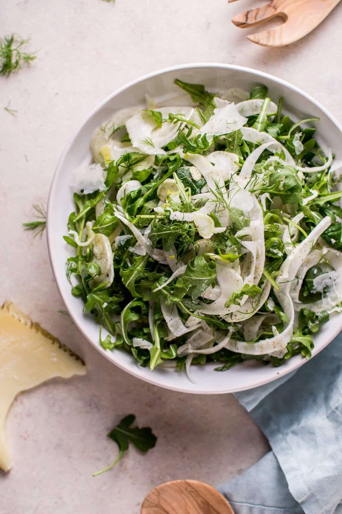 arugula and fennel salad in a bowl beside a piece of Manchego cheese