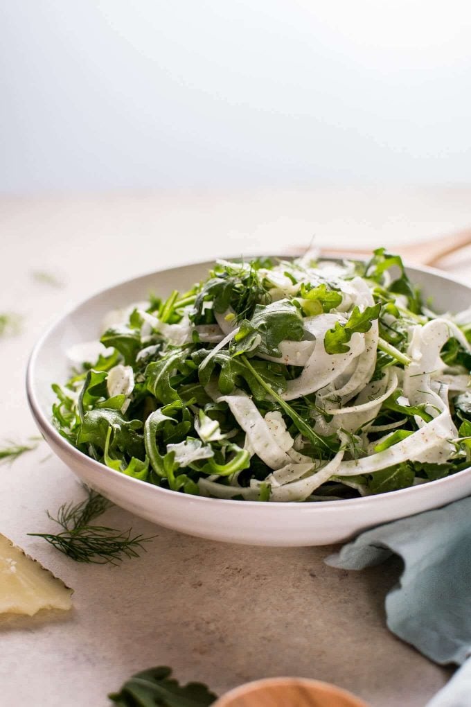white bowl of arugula and fennel salad on a table with dill sprig