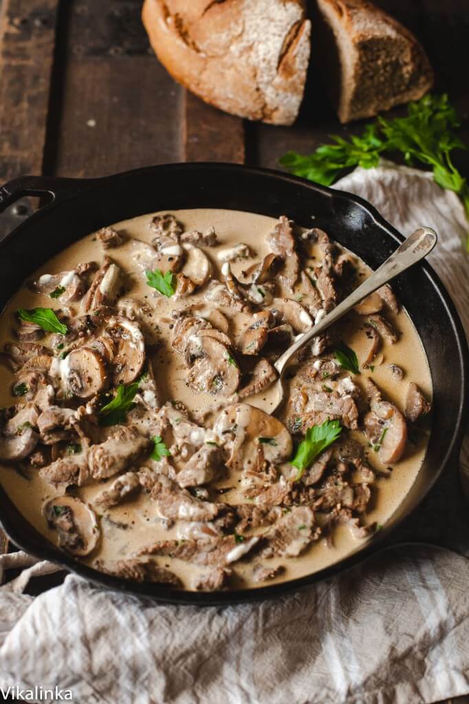 skillet with beef stroganoff and a serving spoon with bread in the background