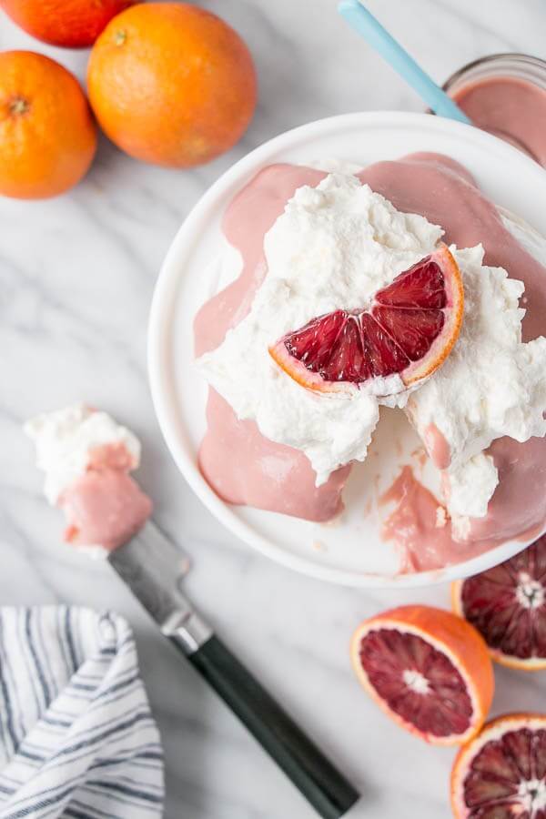 blood orange pavlova with whipped cream in a dish beside oranges and a knife