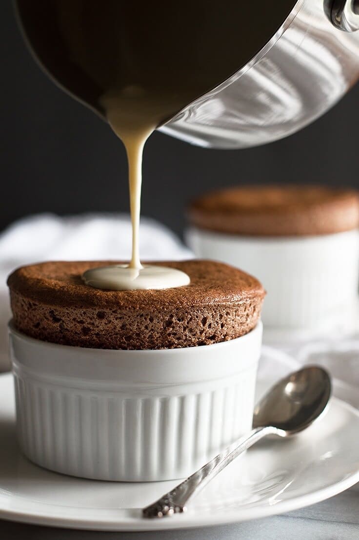 creme anglaise being poured on a chocolate souffle in a small ramekin beside a spoon