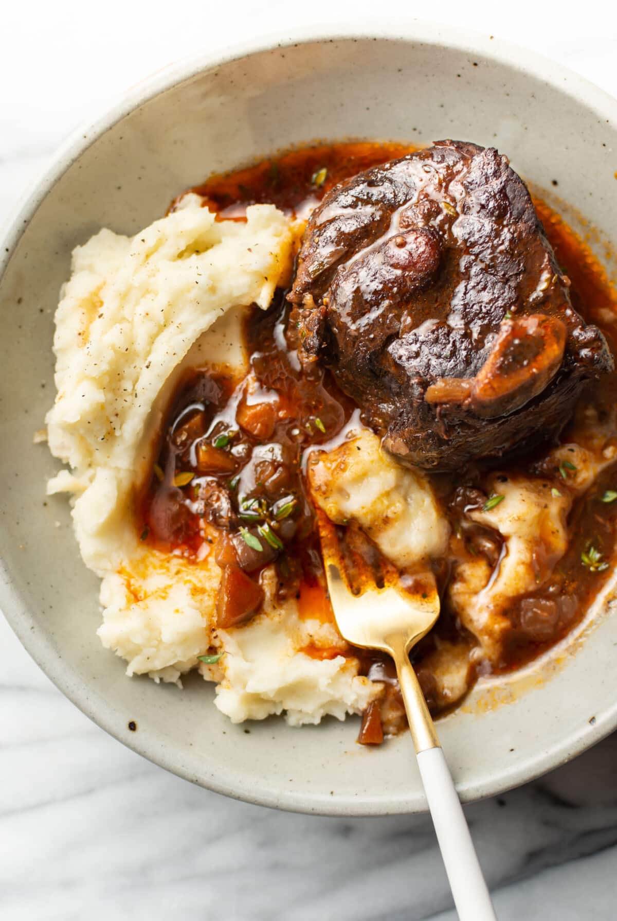 a bowl with crockpot red wine braised short ribs over mashed potatoes with a fork