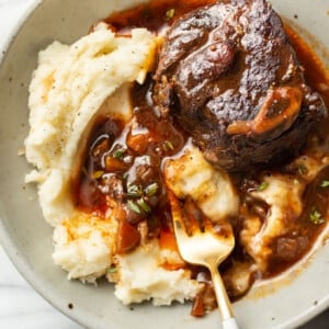 a bowl with crockpot red wine braised short ribs over mashed potatoes with a fork
