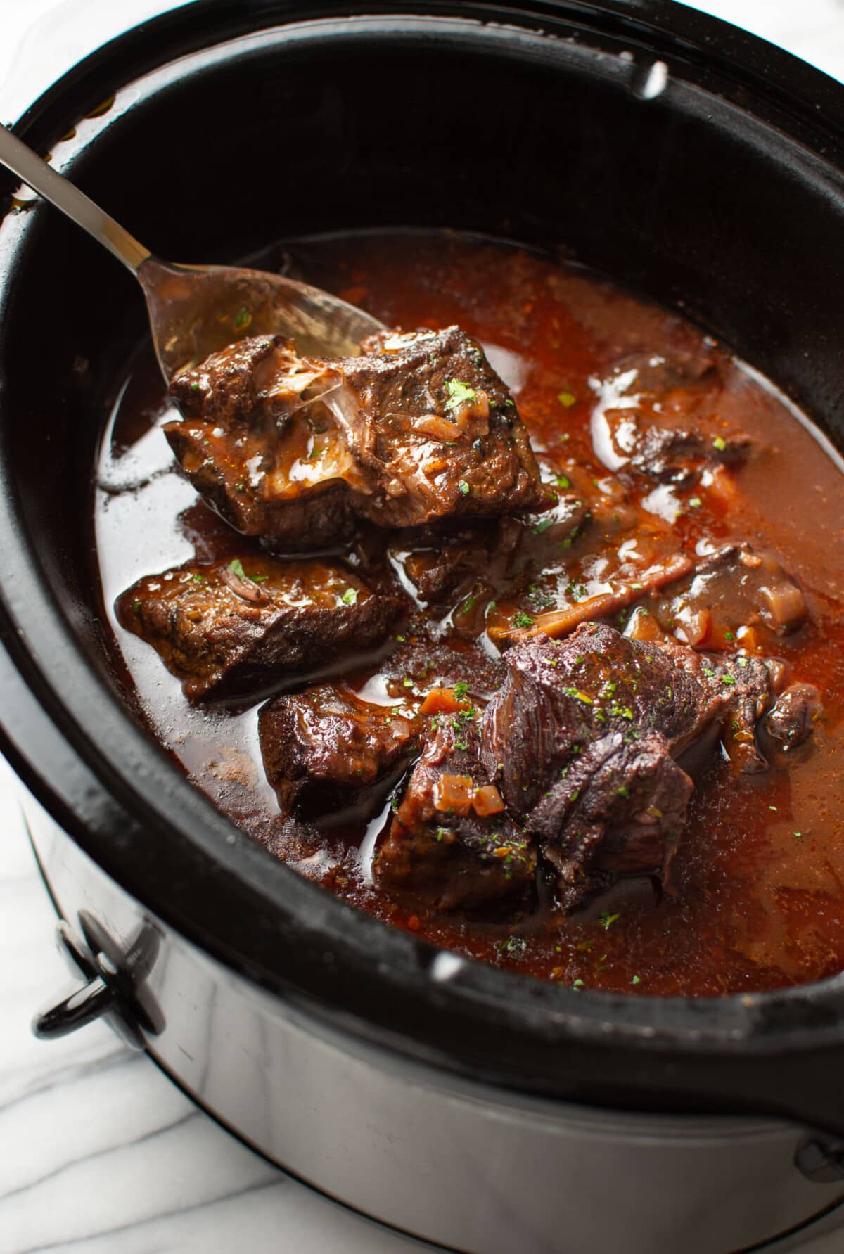 a slow cooker with red wine braised short ribs and a serving spoon