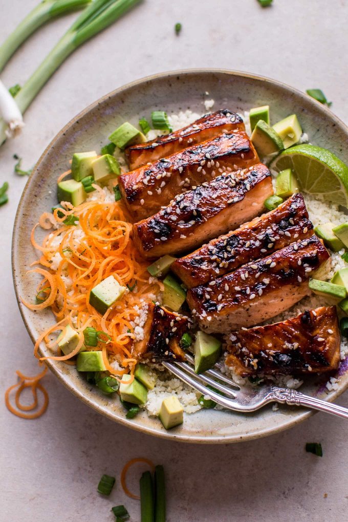glazed salmon with hoisin and sesame seeds in a bowl with cauliflower rice, avocado, and a fork