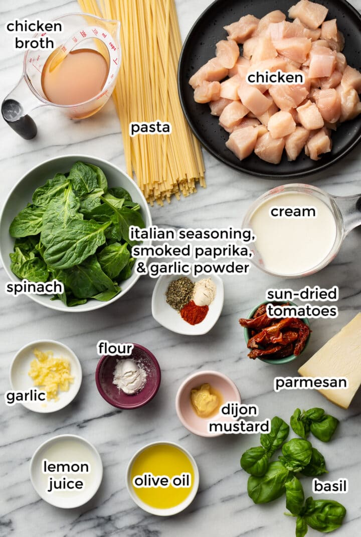 all the ingredients for creamy tuscan chicken pasta in small bowls and plates on a marble surface