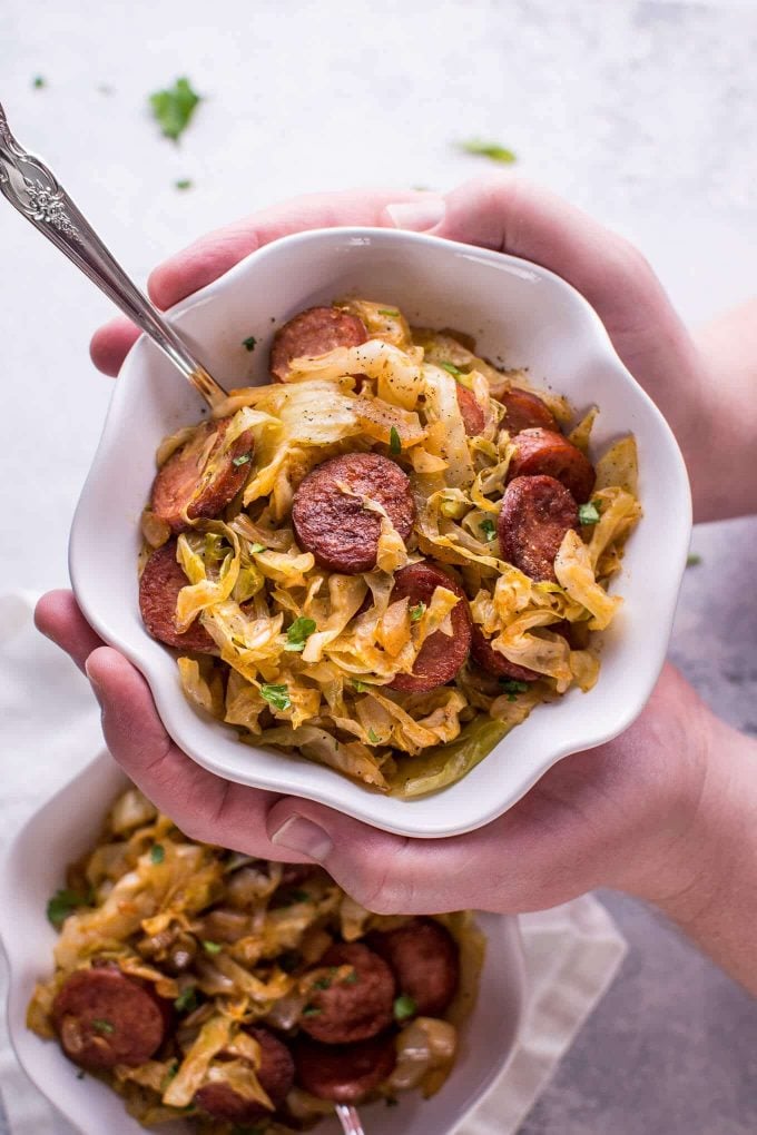 two male hands holding a bowl of sauteed cabbage and kielbasa