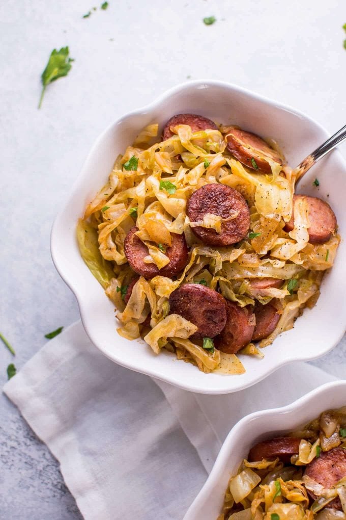 bowl of easy sauteed cabbage and kielbasa sausage with a fork beside cloth napkin
