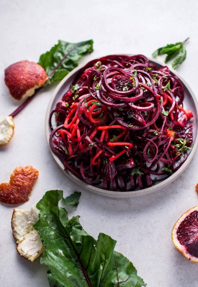 bowl of raw beet and blood orange vegan salad beside orange peels and beet leaves