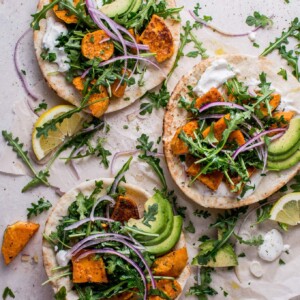 roasted sweet potato pitas with arugula and garlic dressing topped with avocado beside lemon slices