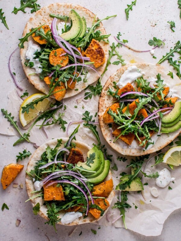 roasted sweet potato pitas with arugula and garlic dressing topped with avocado beside lemon slices