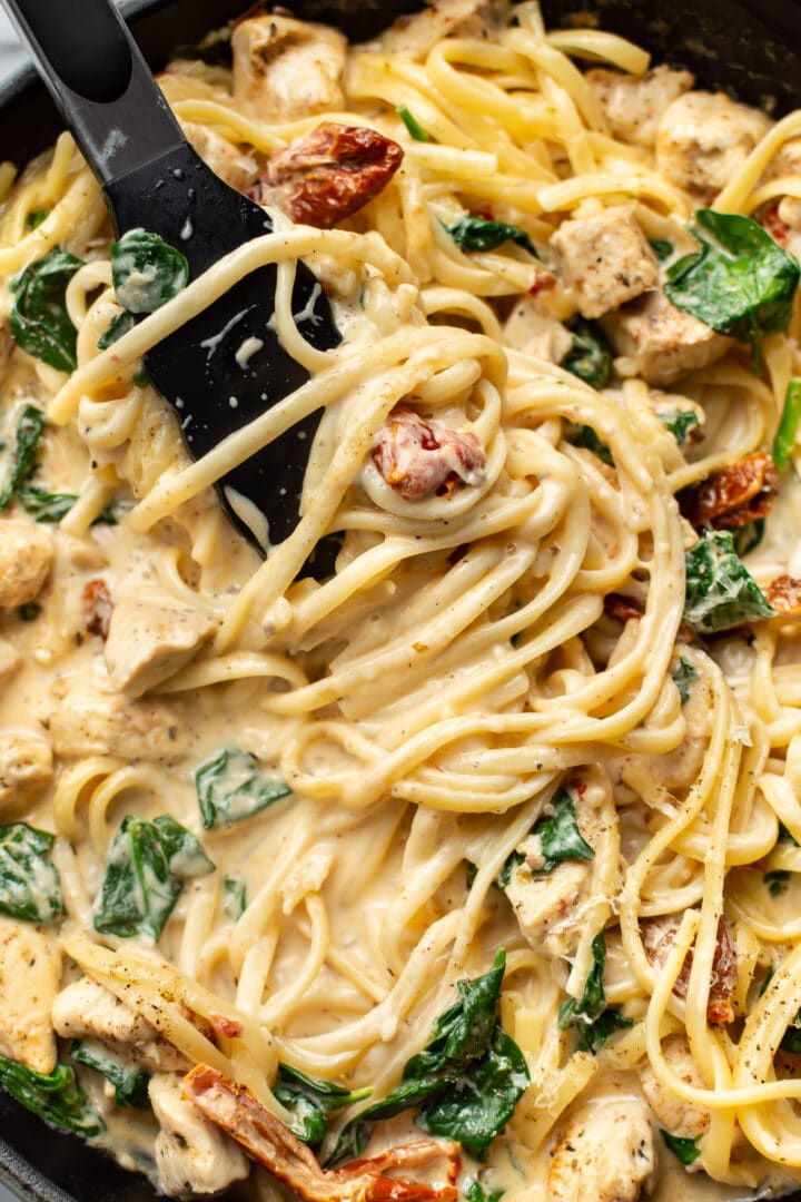 close-up of serving tongs serving tuscan chicken pasta in a skillet