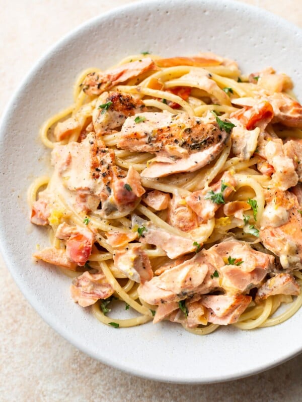 close-up of white bowl with creamy lemon and fresh tomato salmon pasta