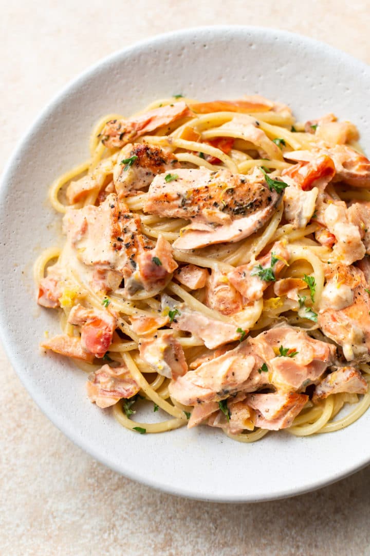 close-up of white bowl with creamy lemon and fresh tomato salmon pasta