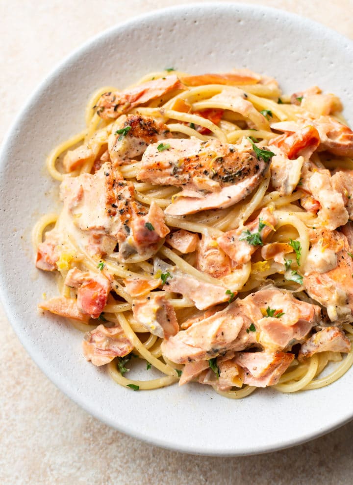 close-up of white bowl with creamy lemon and fresh tomato salmon pasta