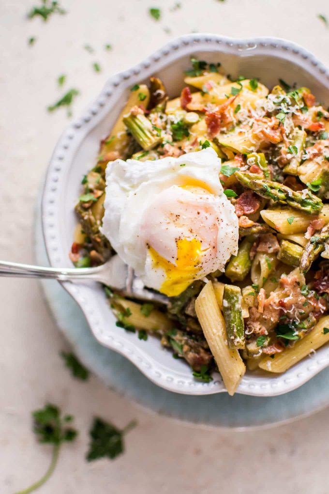 bowl with asparagus and bacon pasta and a poached egg and fork