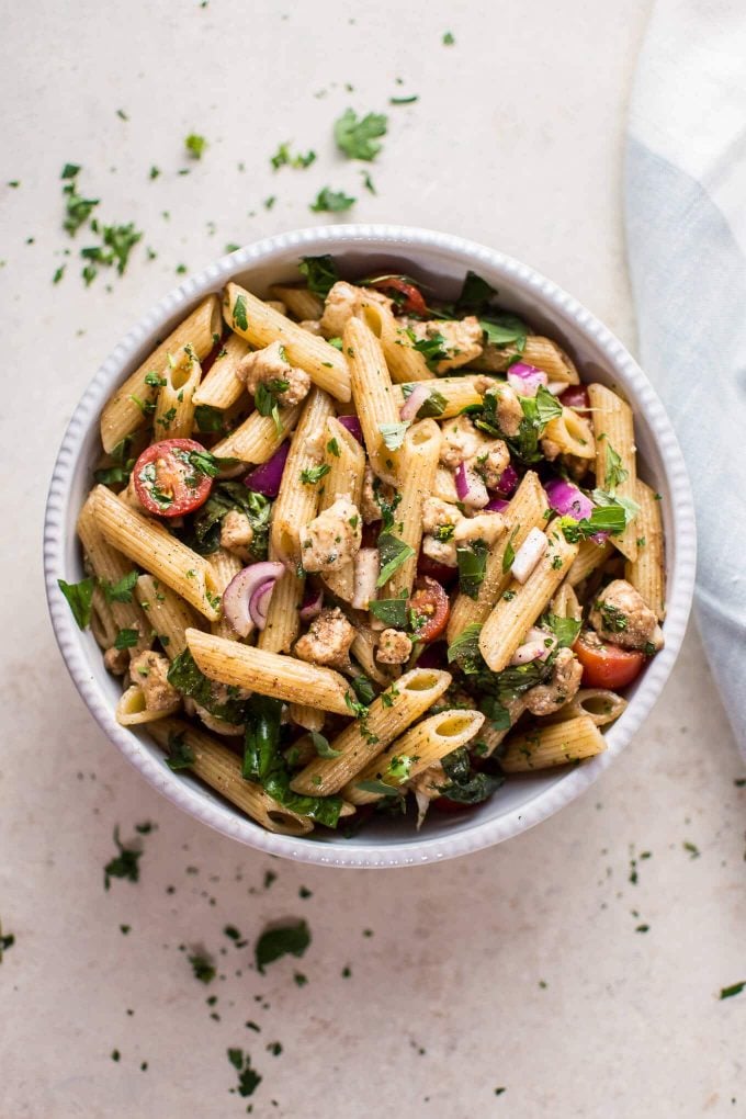 balsamic Caprese pasta salad in a white bowl beside cloth napkin