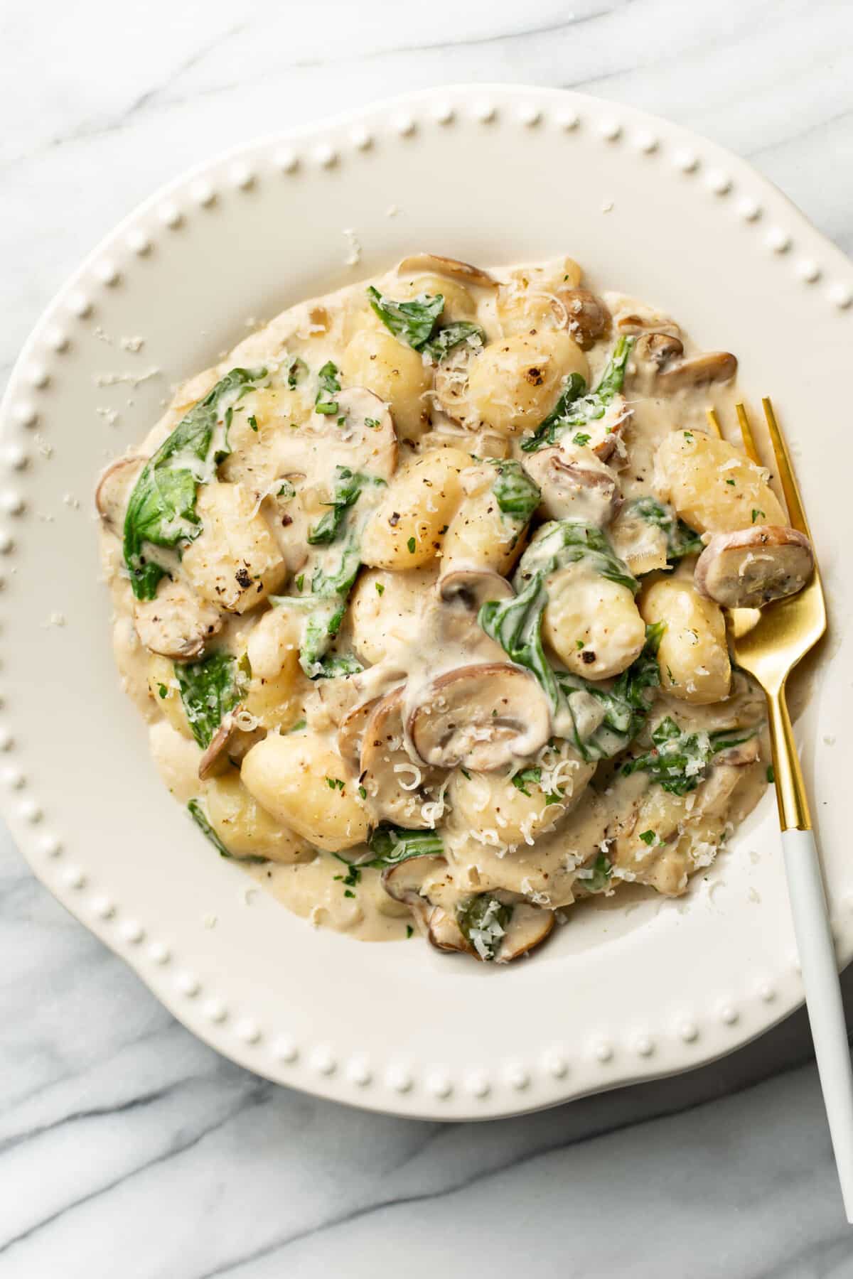 a bowl of creamy mushroom spinach gnocchi with a fork