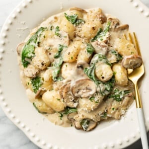 a bowl of creamy mushroom spinach gnocchi with a fork