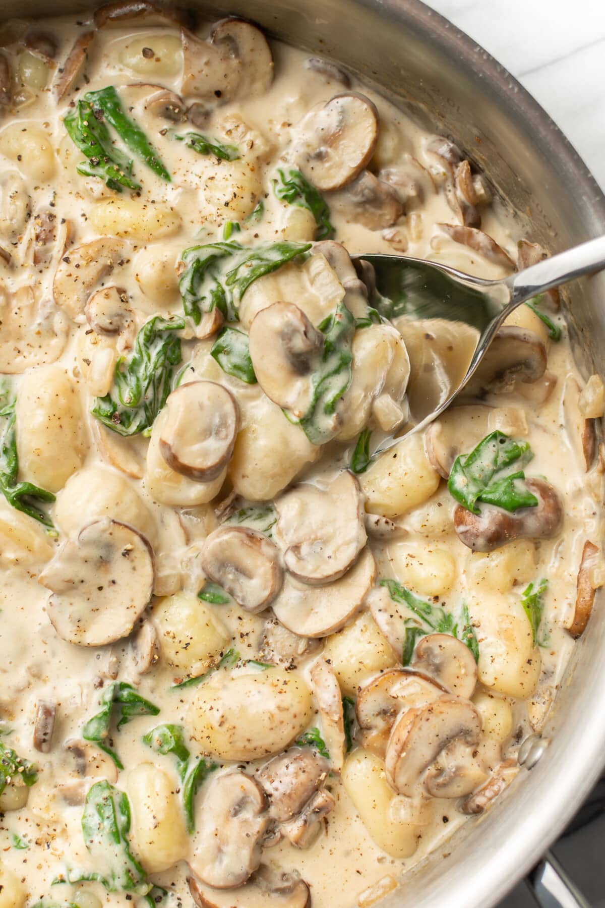 a skillet with creamy mushroom gnocchi and a serving spoon
