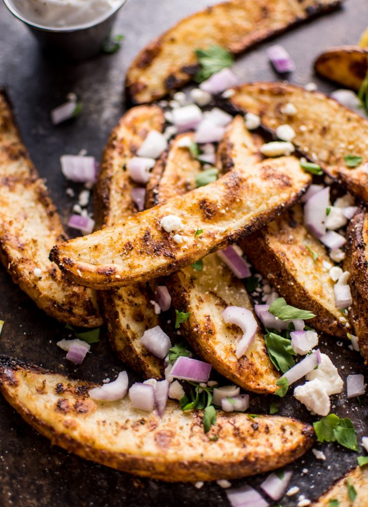These Greek loaded baked potato wedges make a tasty appetizer or side dish. Served with tzatziki for dipping!