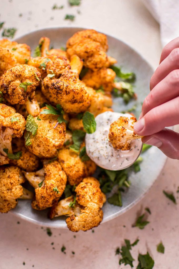a hand dipping a roasted cauliflower bite into container of mint dipping sauce