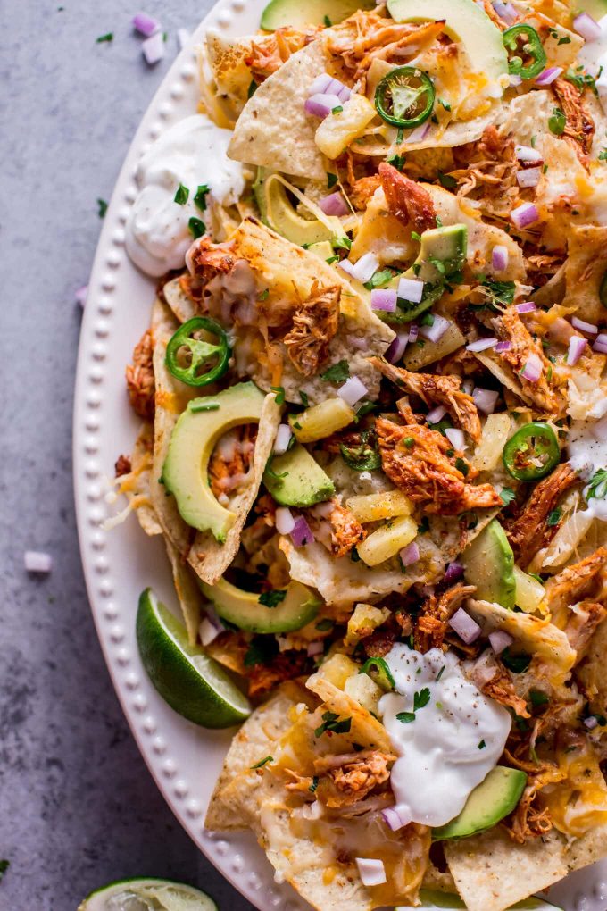 tropical chicken nachos topped with plenty of avocado and sour cream on a plate