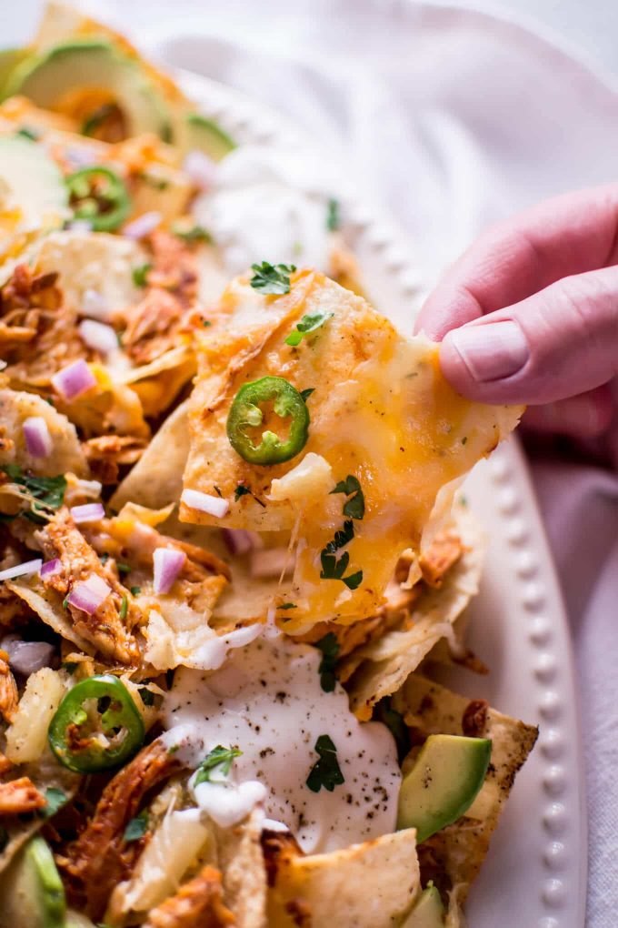 a hand holding tropical chicken nachos