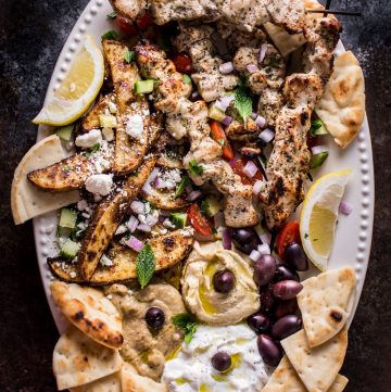 The Ultimate Greek Chicken Souvlaki Platter is loaded with tender grilled chicken skewers, pita bread, Greek potato wedges, hummus, tzatziki, melitzanosalata, kalamata olives, feta, and other goodies. The perfect meze assortment for any feast or party!