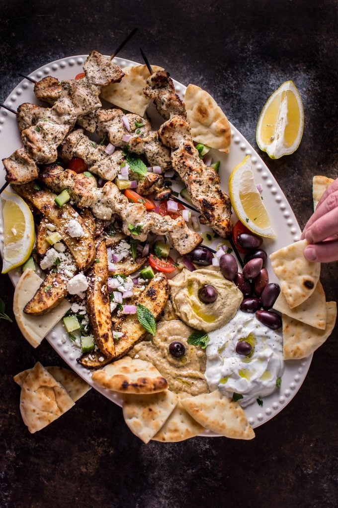 Greek chicken souvlaki platter with chicken skewers, hummus, pita bread, potato wedges, hummus, and more