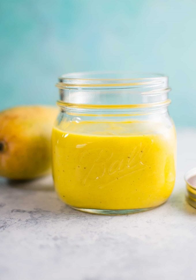 glass mason jar with easy mango salad dressing and whole mango in the background