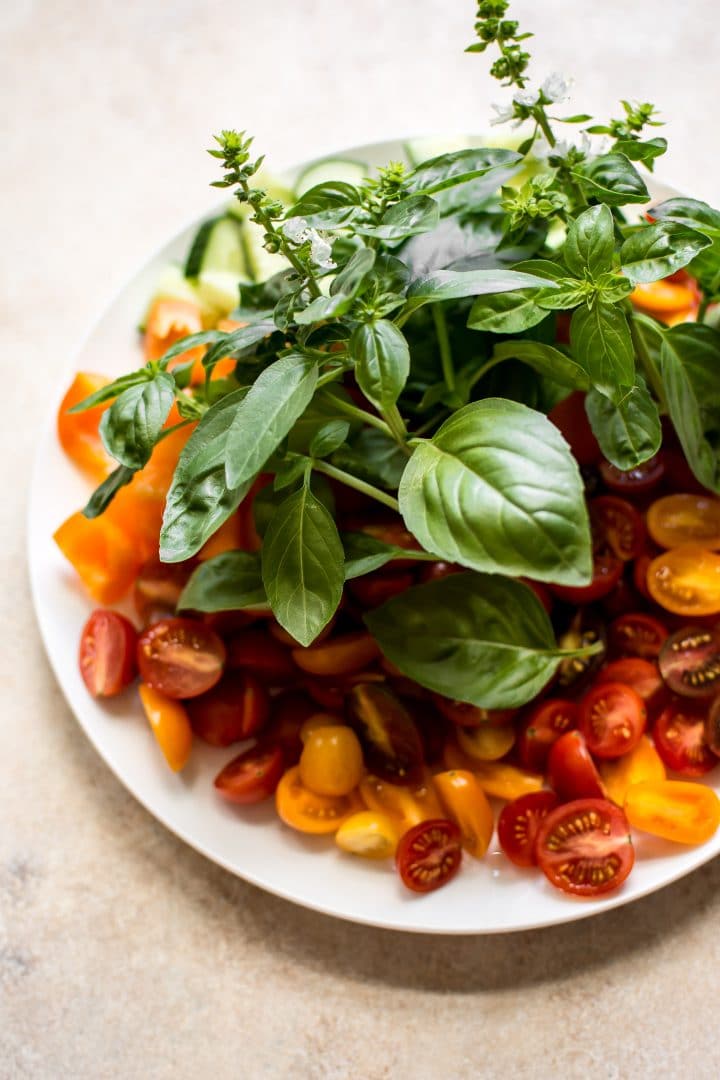 small white plate with orange and red tomatoes and handful of basil