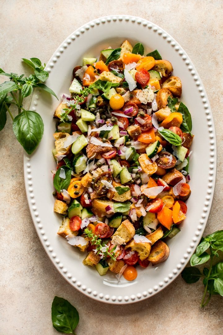 italian panzanella salad on a large oval white serving plate with basil garnish