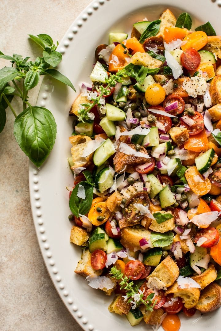 close-up of panzanella salad in an oval white serving bowl with basil garnish