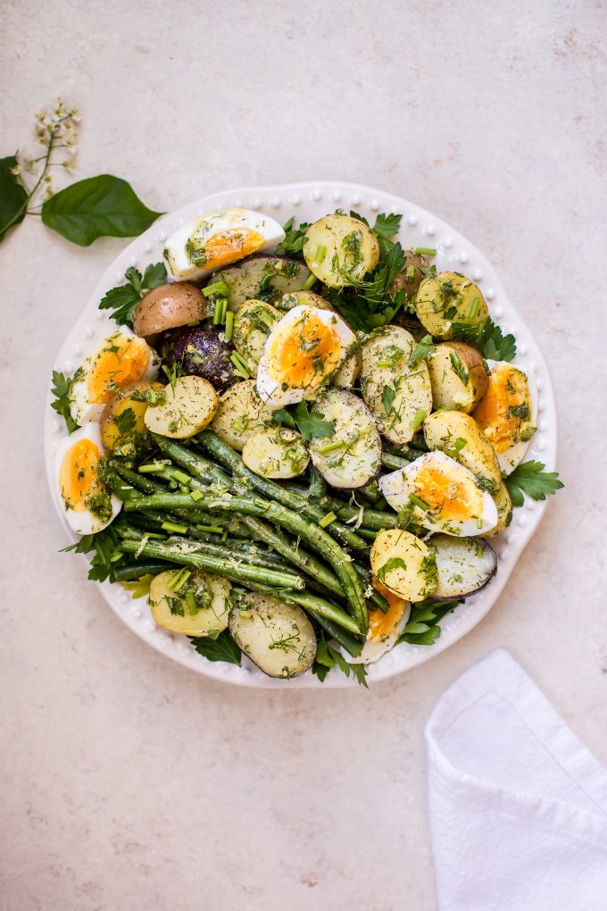 potato and green bean salad with eggs on a plate beside a cloth napkin