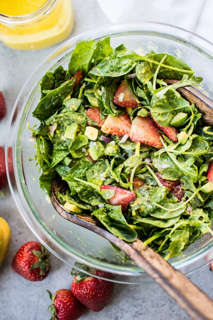 close-up of strawberry spinach salad with mango dressing in a glass bowl with wooden salad utensils
