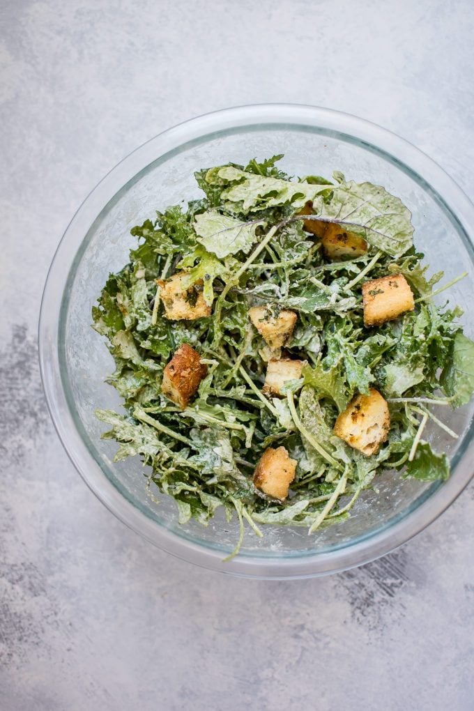 glass serving bowl with baby kale salad with lemon tahini dressing and homemade garlic parmesan croutons