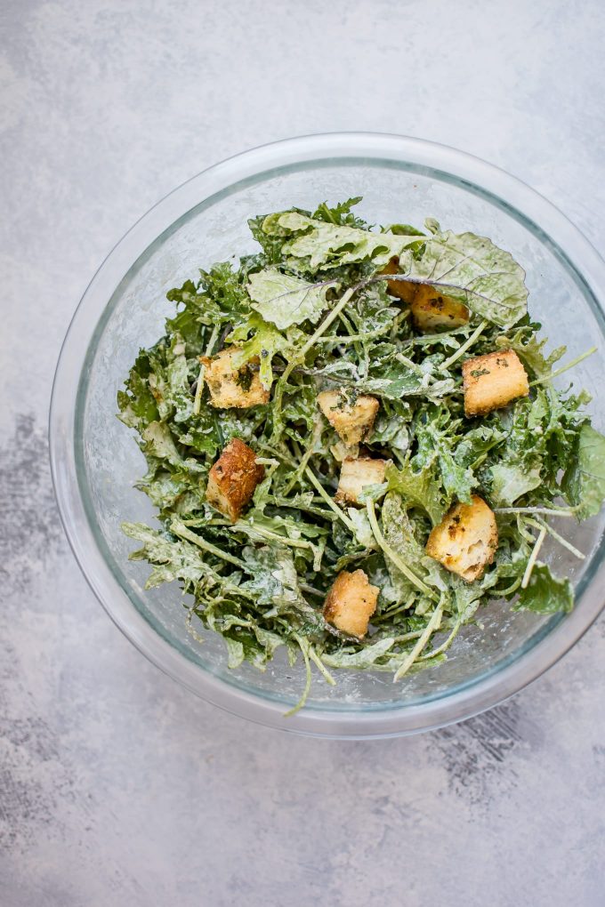 glass serving bowl with baby kale salad with lemon tahini dressing and homemade garlic parmesan croutons