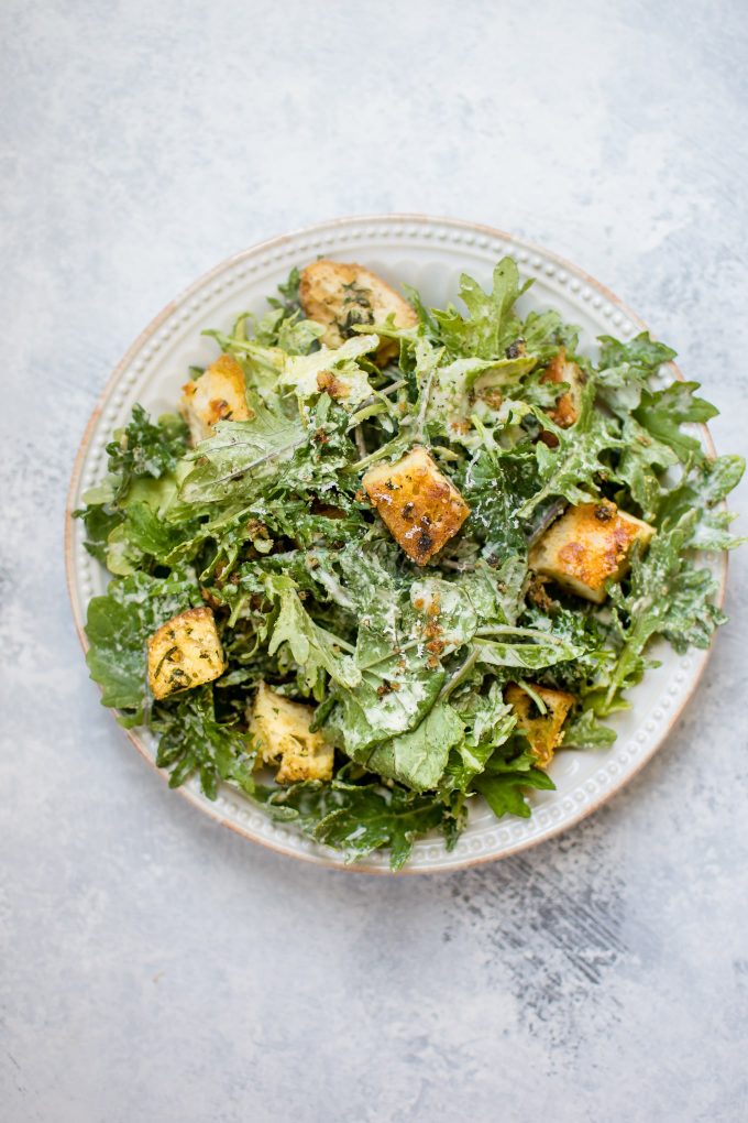 white plate with baby kale salad with lemon tahini dressing and homemade garlic parmesan croutons