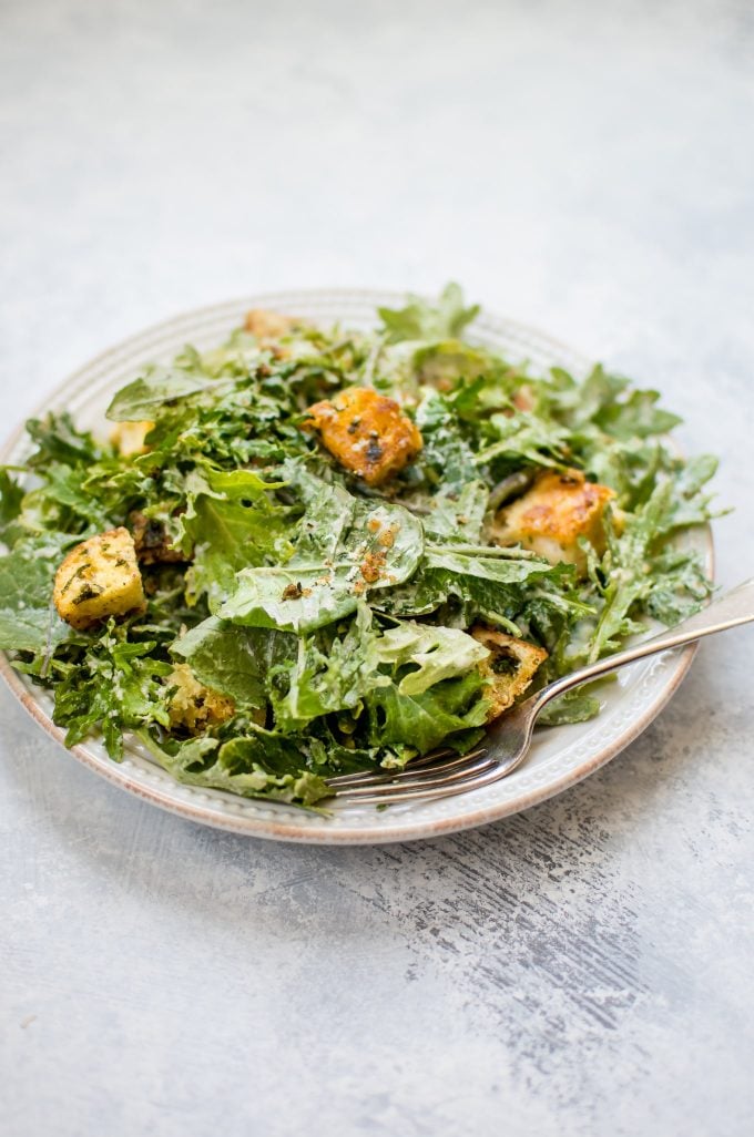 plate with baby kale salad with lemon tahini dressing and homemade garlic parmesan croutons and a fork